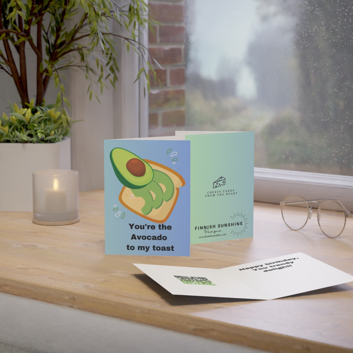 Photo displays the card which features a picture of avocado toast on the front, accompanied by the phrase "You're the Avocado to My Toast." Image includes photo of back of card and an opened card with text and QR code